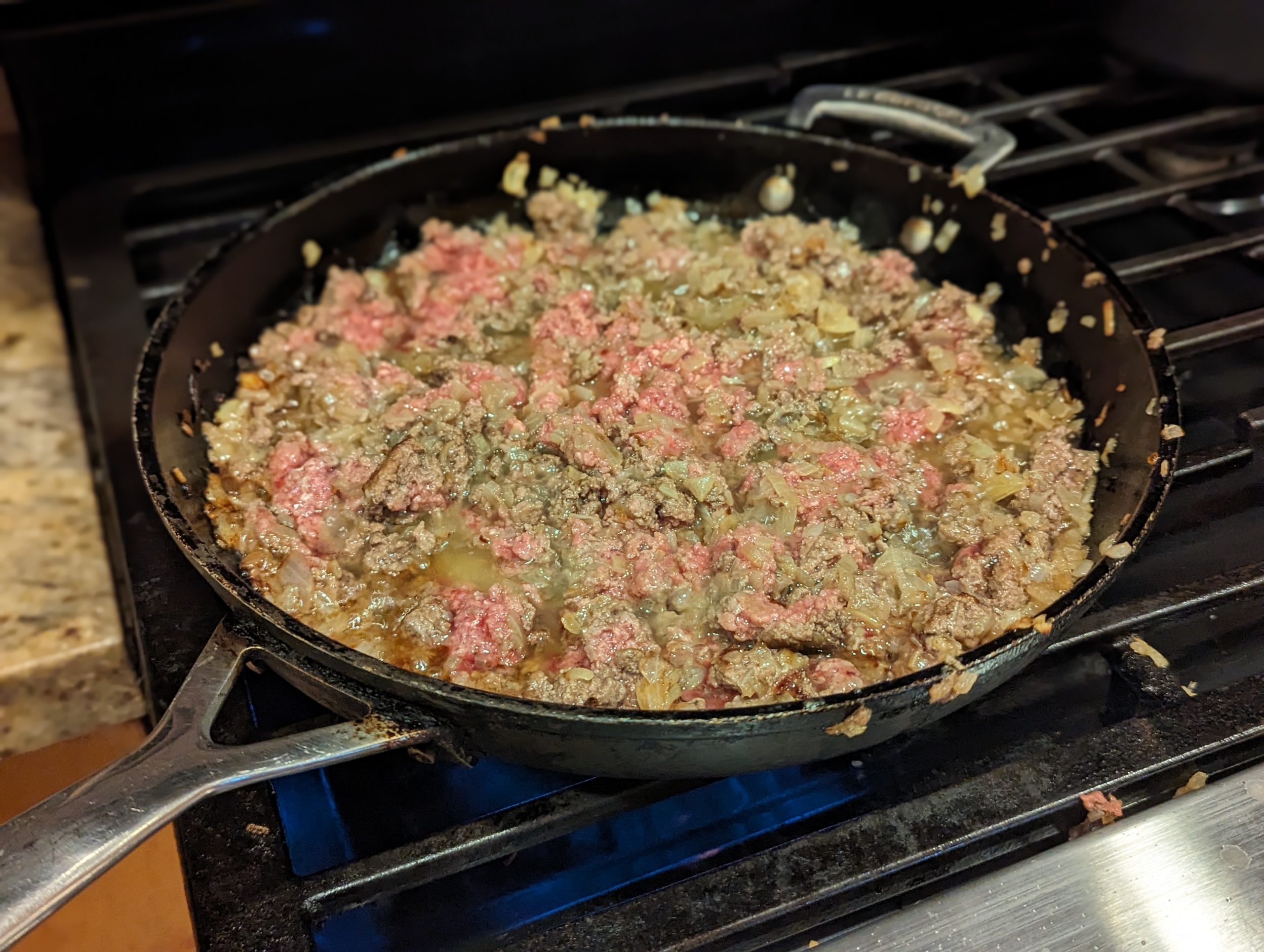 Ground beef frying in a frying pan with onions and shallots