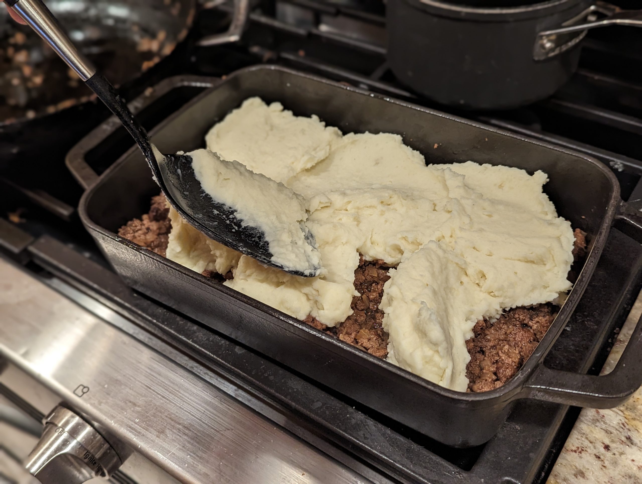 Preparing Hachis Parmentier Sheperd's Pie in a casserole baking dish with mashed potatoes layered over ground beef