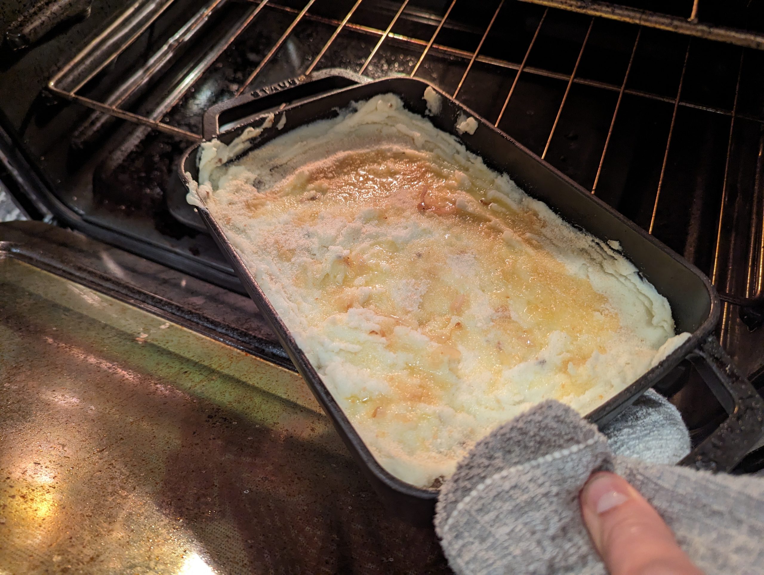 Getting the Hachis Parmentier Sheperd's Pie out of the hot oven with an oven mitt.